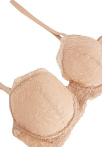 Béžová krajková podprsenka s vycpanými košíčky, květinovým vzorem, vlnitým okrajem a nastavitelnými ramínky. Měkká textura a hladký povrch.