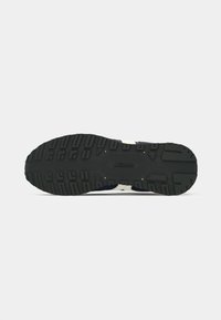 Sort gummisåle til sneakers med teksturerede dæk- mønstre, der har et glat centralt område og diskret branding. Hvite accenter på siderne.