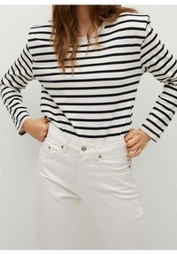 Camiseta de manga larga a rayas en blanco y azul marino, combinada con pantalones vaqueros blancos que tienen un cierre de botón y dos bolsillos con detalles de cobre.