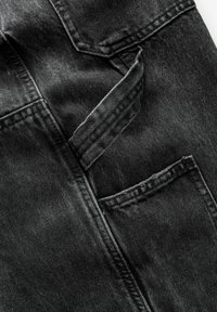 Gros plan sur un jean en denim noir plié montrant les coutures détaillées et la texture du tissu sur les poches et les coutures.