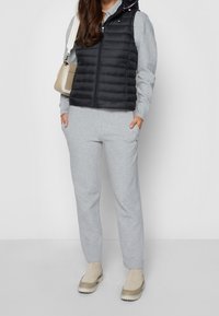 Svart puffy väst med huva över en grå sweatshirt och matchande sweatpants. Beige plattformsskor och en liten beige handväska.