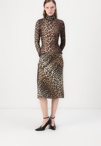 Haut à col roulé en imprimé léopard et jupe crayon assortie dans des nuances de marron, présentant des tissus lisses et une silhouette ajustée. Talons noirs à bride de cheville.