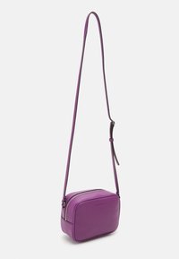 Piccola borsa a tracolla rettangolare viola con tracolla regolabile e chiusura con zip, logo di Calvin Klein Jeans in rilievo sulla parte frontale.