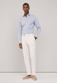 Camisa de botones a rayas azul claro, pantalones blancos de corte slim y zapatos slip-on de ante beige. Texturas suaves y diseño sencillo.
