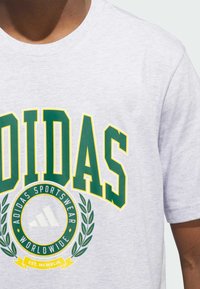 Pilkas medvilninis marškinėlis su ryškiu žaliu ir geltonu "ADIDAS" užrašu, apskritu logotipu su laurų dizainu ir tekstu "EST. MCMXLIX".