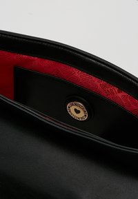 Svart läderväska med röd tygfoder som har trycket "LOVE MOSCHINO" samt en rund metallknapp med varumärket och ett hjärta.