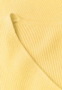 Gros plan d’un tissu côtelé jaune doux avec une couture formant un pli diagonal à travers le matériau.