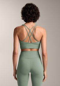 Mintgroene sportbeha en high-waisted legging met een crisscross bandontwerp op de rug. Glad textuur, minimale branding op de tailleband.