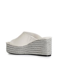 Mules compensés en cuir blanc avec un design en fil métallique argenté superposé sur le talon, présentant un bout ouvert et une texture supérieure lisse.