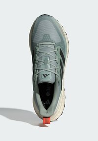 Svetlozelené bežecké topánky s hornou časťou z vrstvenej textílie, čiernymi pruhmi, textúrovanou podrážkou a červeným akcentom na päte. Obsahujú zabezpečený systém šnurovania.