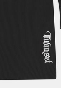 Tessuto nero a coste con il testo ricamato in bianco "Unself" in carattere gotico vicino al bordo, su uno sfondo bianco.