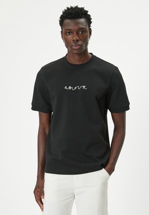 Sort bomulds t-shirt med korte ærmer, prydet med en hvid kursiv "amour" design på forsiden. Rund halsudskæring, afslappet pasform.