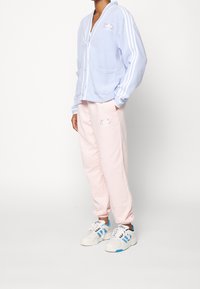 Light blue fleece cardigan with white stripes, button closure, and pockets. Soft pink sweatpants featuring embroidered design. White sneakers with blue accents.
