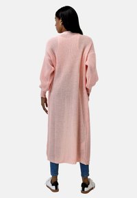 Lång, lätt, stickad cardigan i mjuk rosa, med en lös passform och vida ärmar. Bärs med jeans och avslappnade sneakers.