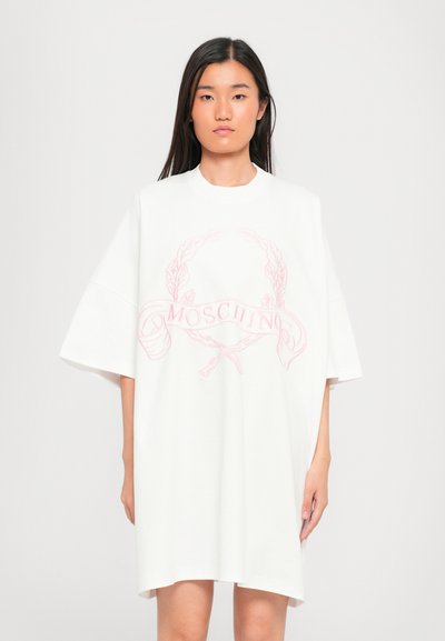Bílé oversized tričkov dress s růžovým logem Moschino, které zahrnuje vavřínový věnec a stužkové akcenty. Hladká bavlněná látka.