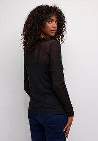 Haut à manches longues noir avec panneau arrière en dentelle, encolure ronde et coupe ajustée. Associé à un jean bleu foncé, mettant en valeur une texture lisse.