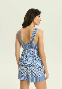 Niebieski i biały romper w wzory z dopasowaną górą, szerokimi paskami i rozkloszowanym, warstwowym wykończeniem peplum. Szorty mają pasek na dolnej krawędzi.