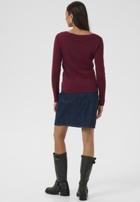 Bordeaux langemouwen top met een brede halslijn, gecombineerd met een denim rok en zwarte kniehoge laarzen met banden en gespen.