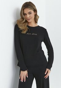 Czarna bluzka z długim rękawem wykonana z miękkiej tkaniny, z haftem "Mon Amie" w złotym kolorze. Charakteryzuje się luźnym krojem i przeszyciami na rękawach.