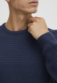Marineblauer gestrickter Pullover mit einem strukturierten Muster, geripptem Rundhalsausschnitt und langen Ärmeln mit gerippten Bündchen.