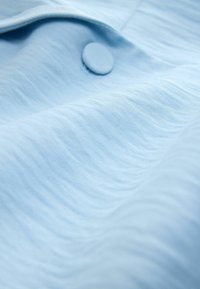 Tissu bleu clair avec un fin côtelé horizontal et un bouton recouvert cousu près d'une couture ou d'un pli.