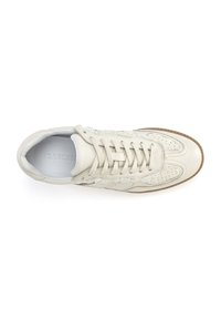 White leather sneaker with perforated detailing, flat laces, and a textured rubber sole. Features subtle stitching accents and a rounded toe.
