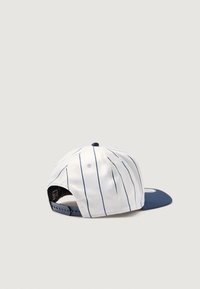 Biela čiapka s úzkymi modrými pruhmi, zakriveným námořníckym okrajom, nastaviteľným snapback uzatváraním a tkaninovou etiketou vo vnútri.