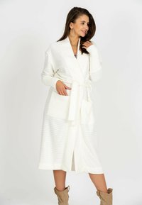 Długa, biała szata z prążkowanej tkaniny z paskiem w talii, z dwoma przednimi kieszeniami i szerokim kołnierzem.