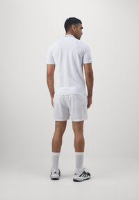 Camisa polo blanca de manga corta, combinada con pantalones cortos blancos. El conjunto incluye calcetines deportivos blancos y zapatillas negras y blancas.