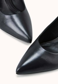 Escarpins pointus en cuir noir, à la texture lisse, au design épuré et aux côtés ouverts, offrant une esthétique raffinée et minimaliste.