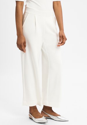 Weisse weite Hosen mit glatter Textur, ausgestattet mit vorderen Falten und seitlichen Taschen. Kombiniert mit silbernen spitzen Ballerinas.