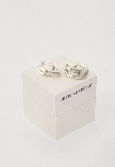 Ασημί στρογγυλά σκουλαρίκια σε σχήμα βρόχου, τοποθετημένα σε ένα λευκό κουτί με το λογότυπο "Charlotte CHESNAIS". Λείος επιφάνεια με γυαλιστερό φινίρισμα.