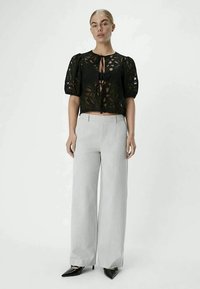 Black lace crop top with puff sleeves, featuring a tie-front closure; paired with light gray pinstriped wide-leg trousers and black pointed heels.