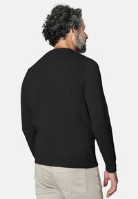 Suéter negro de manga larga con puños y dobladillo acanalados, que presenta un escote redondo. Se muestra desde la parte posterior en una persona con pantalones de color claro.