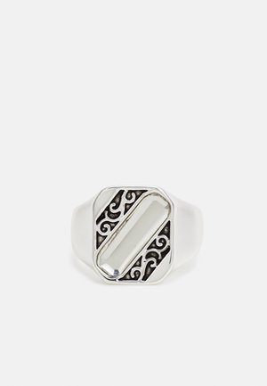 Anel em tom prateado com uma pedra retangular clara e um intricado design em filigrana preta, apresentando uma banda lisa com um acabamento polido.