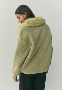 Roheline kunstkarvase mantel, millel on pehme ja tekstuuriga välimus ning sobituv karvakaelus. Omab lõdvestunud istuvust ja langetatud õlgu.