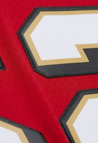 Tissu de sport rouge avec un grand numéro blanc et noir entouré d'or. Le gros plan met en évidence la texture des coutures et le design perforé.