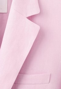 Blazer en lin rose clair montrant le col, le revers et une petite poche poitrine sur un tissu texturé.