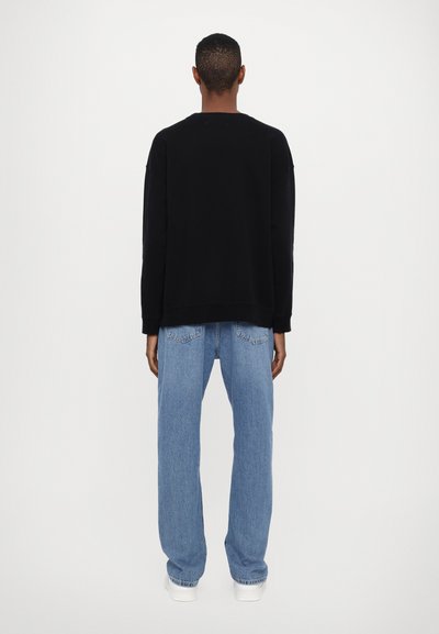 Un sweat à capuche noir avec des épaules tombantes, associé à un jean droit bleu clair. L'ensemble présente une coupe décontractée et un design simple.