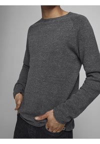 Szary sweter z długim rękawem, wykonany z fakturowanej tkaniny, z okrągłym dekoltem i ściągaczami, noszony na ciemnych dżinsach.