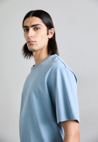 Camiseta de manga corta azul claro, hecha de tejido suave, con cuello redondo y corte relajado, con textura suave y costuras mínimas.