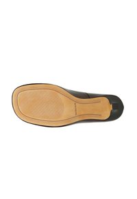 Suola di scarpa in pelle nera con una superficie liscia e leggermente strutturata. Suola in gomma color sabbia con scanalature per trazione e un logo discreto.