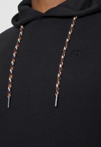 Sort hætte sweatshirt med en tekstureret snor i orange, navy og hvidt flet, samt et lille logo på brystet.