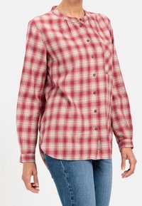 Chemise à manches longues à carreaux rouges et blancs avec col mao, boutonnée sur le devant, poche poitrine et fentes latérales ; fabriquée en tissu léger et texturé.