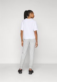 T-shirt bianco a maniche corte, vista posteriore, abbinata a pantaloni della tuta grigi chiari e sneakers nere, caratterizzata da un design semplice e rilassato.
