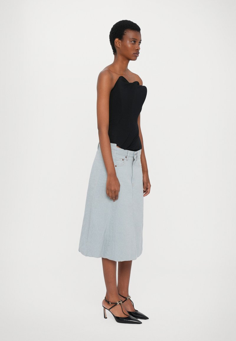 Schwarzer trägerloser Body, hellblauer Jeansrock mit Taschen und schwarze spitze High Heels mit Knöchelriemen. Sanfte Texturen und taillierte Passform.