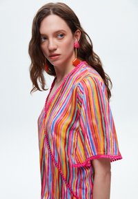 Farverig stribet kimono med levende nuancer af pink, orange og blå, med pom-pom kant langs kanterne og løse ærmer.