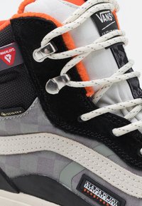 VANS vysoké tenisky v černé, šedé a oranžové barvě. Mají semišové a textilní materiály, bílé tkaničky a výrazné značkové detaily.