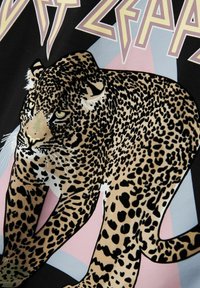Svart tyg med ett leopardsgrafik i beige och svart med gröna accenter, mot pastellfärgade geometriska former. Texten ovanför lyder "LED ZEPPELIN."