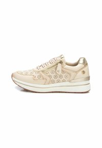 Zapatilla beige con diseño perforado, acentos dorados y un zipper lateral. Cuenta con un collar acolchado y una suela blanca acolchada para mayor soporte.